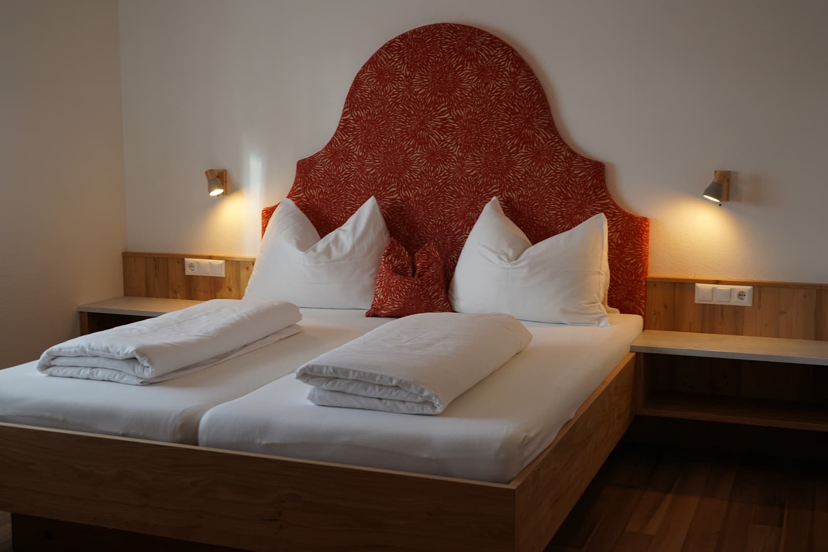 Gemütliches Doppelbett mit rotem Polsterkopfteil im Bucheggerhof